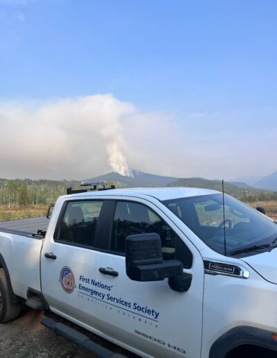 White FNESS pickup truck in foreground. Background is a wildfire on a mountain.