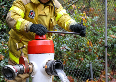 Youth in firefighting gear turning on the fire hydrant.