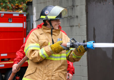 Student firefighter holding the fire hose and smiling.