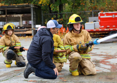 student in firefighting gear learning how to use hose. he's happy and smiling.