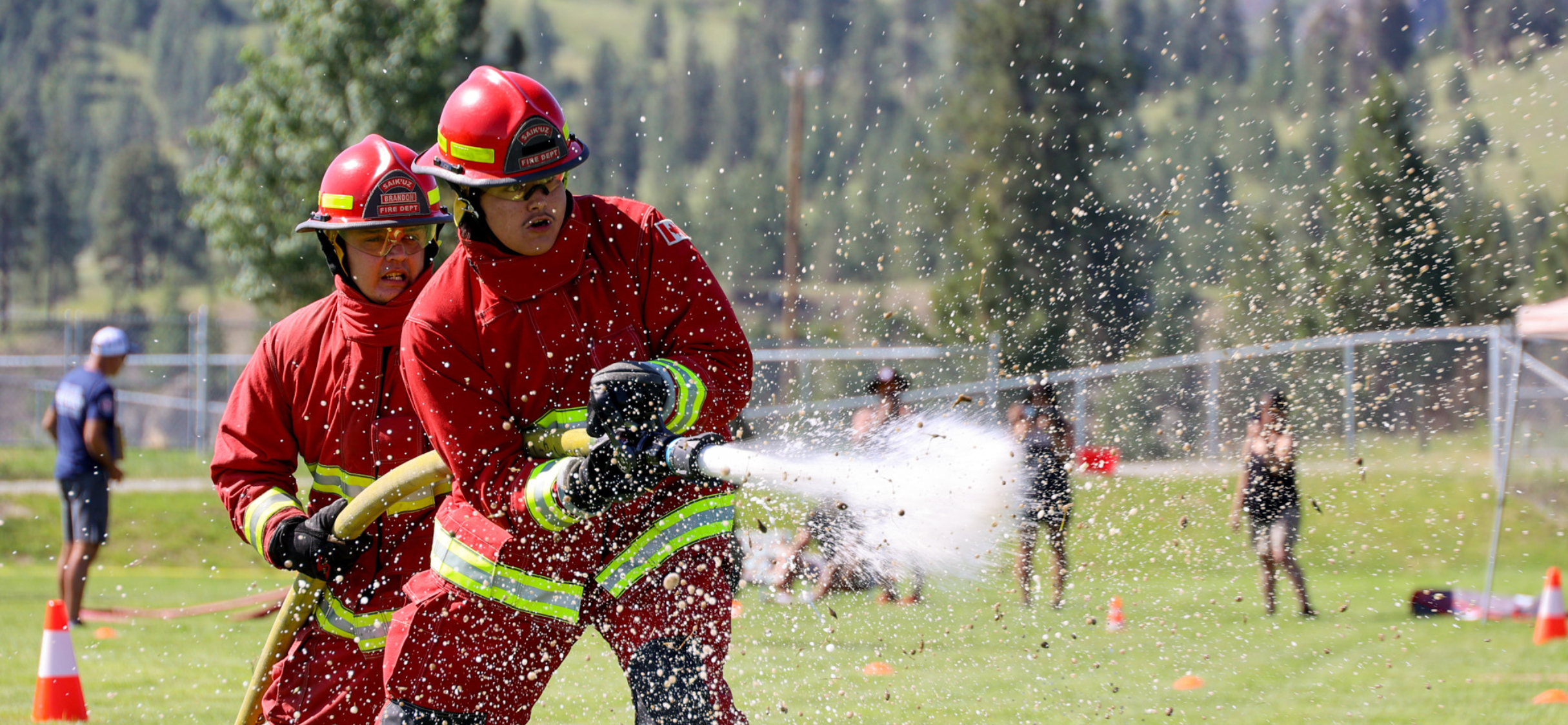 two indigenous firefighters holding a fire hose